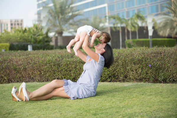 Mutter mit Baby sitzen auf einem Rasen. Die Mutter hält das Baby in die Luft